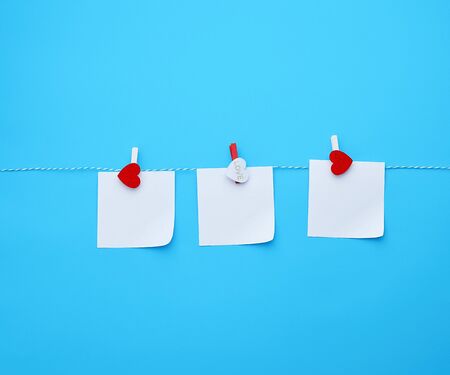 three empty square white paper sheets hanging on decorative clothespins, blue background