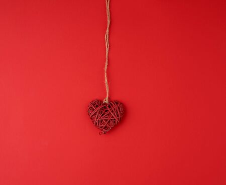 red wicker decorative heart hanging on brown rope, red festive background for Valentine's day