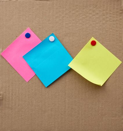 blank square sheets of paper stickers attached with an iron button on a brown cardboard surface....