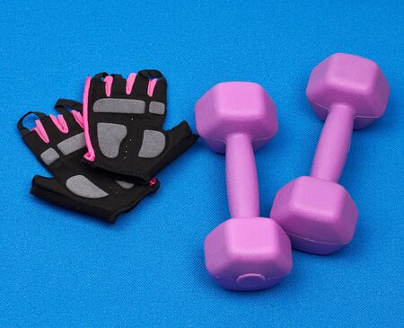 pair of purple plastic dumbbells, gloves on a blue neoprene mat, top view, training equipmentの写真素材