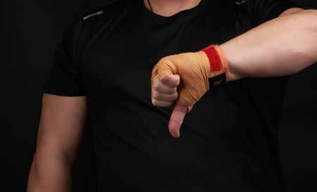 adult athlete in black uniform and hands rewound with textile orange bandage shows gesture dislike,...