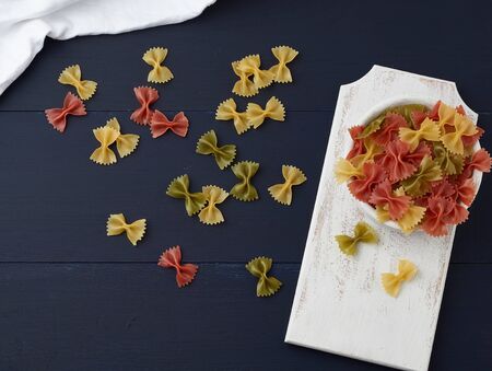 raw pasta in the form of bows in a wooden round plate and white textile napkin on a blue wooden...