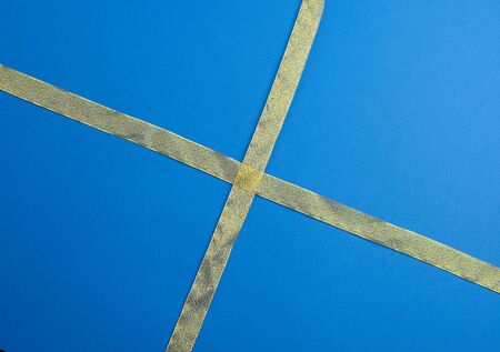 golden silk ribbon crossed on a dark blue background, imitation of tying a gift, top viewの写真素材