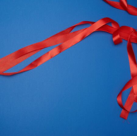 red silk thin ribbon twisted on a blue background, top viewの写真素材