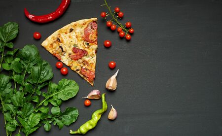 triangular piece of baked pizza with mushrooms, smoked sausages, tomatoes and cheese, black background, flat lay, copy spaceの写真素材