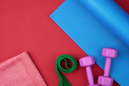 pair of purple plastic dumbbells, green elastic and pink terry towel on a blue neoprene mat, top...