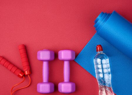 pair of purple plastic dumbbells, bottle of water  on a red neoprene mat, top view, training equipmentの写真素材