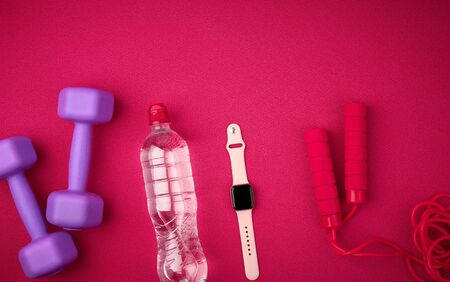 smart watch, bottle of water, red jump rope and lilac dumbbells on a red background from a mat for yoga, top view, sports backdropの写真素材