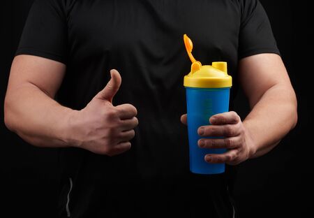 adult male athlete with muscles holds a plastic bottle of water, concept of drinking water in sports and fitness, black backgroundの写真素材