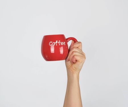 red ceramic cup in a female hand on a white background, hand is raised up