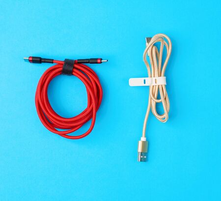 twisted cable for charging mobile devices in a red and golden textile wrapper on a blue backgroundの写真素材