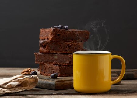 yellow ceramic cup with coffee and a stack of baked brownie pieces on a wooden tableの写真素材
