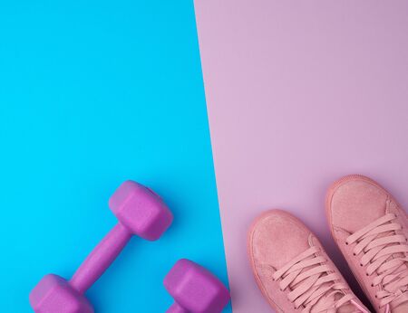 pair of pink leather sneakers, plastic dumbbells for sports on a pink blue background, sports...
