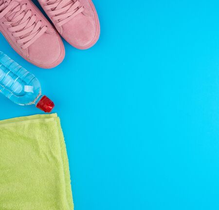folded green terry towel and a transparent bottle of water, pink shoe on a blue background, concept of drinking more water while doing sports, copy spaceの写真素材