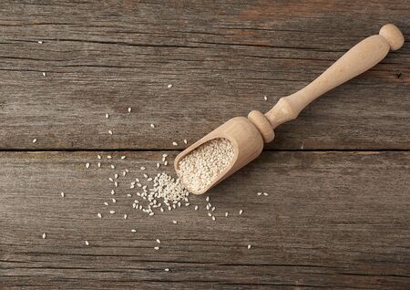 dry white sesame seeds in a brown wooden spoon on a gray wooden table from old boards, top viewの写真素材