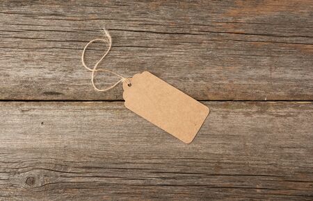 Empty brown paper tag tied with white string. Price, gift, sale tag on the gray wooden background,...