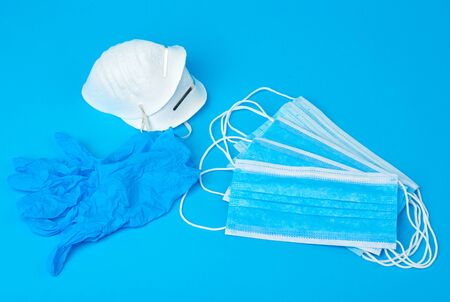 disposable gloves and stack of medical masks made of non-woven material with white rubber bands on a blue background, protective accessory for the respiratory tract from the virus, setの写真素材