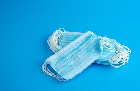 stack of medical masks made of non-woven material with white rubber bands on a blue background,...