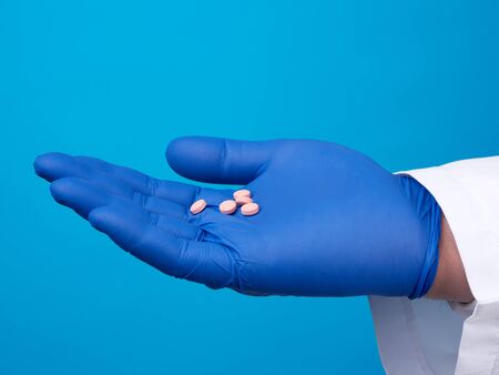 male hand with blue sterile gloves holds round pink pills, concept of drug treatment for diseases,...