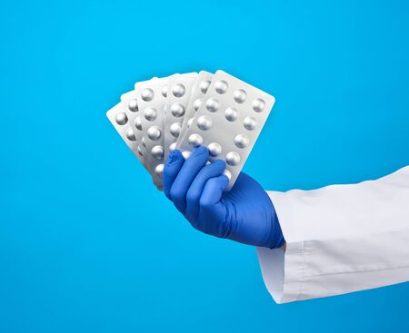 male hand with blue sterile gloves holds a pills in a blister, concept for drug treatment of...