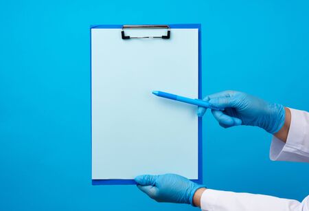 female doctor's hands in blue medical latex gloves holds a folder with a paper clip and a plastic pen, place for writing a diagnosis, messageの写真素材