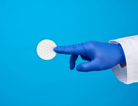 hand hold white cotton round disc for cosmetic procedures on a blue background, close up