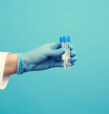 doctor in a white coat and blue sterile latex gloves holds a plastic jar for stool analysis, blue...