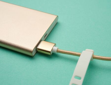 golden power bank and cord with a usb connector for recharging mobile devices on a green background, top viewの写真素材