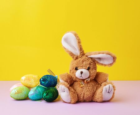 cute rabbit toy and decorative Easter eggs with sequins on a yellow background, festive backdropの写真素材