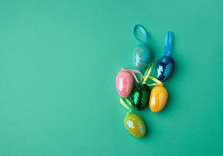 multicolored decorative Easter eggs decorated with sequins on a green background, festive green...