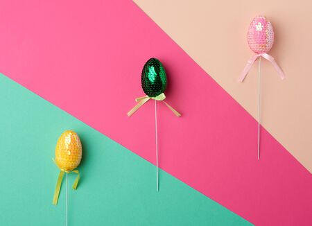 multicolored decorative Easter eggs decorated with sequins on a color background, festive backdrop, top viewの写真素材