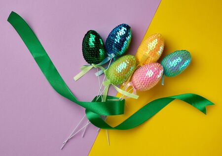 multicolored decorative Easter eggs decorated with sequins on a color background, festive backdrop,...