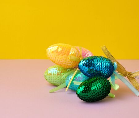 multicolored decorative Easter eggs decorated with sequins on a color background, festive backdrop, top viewの写真素材