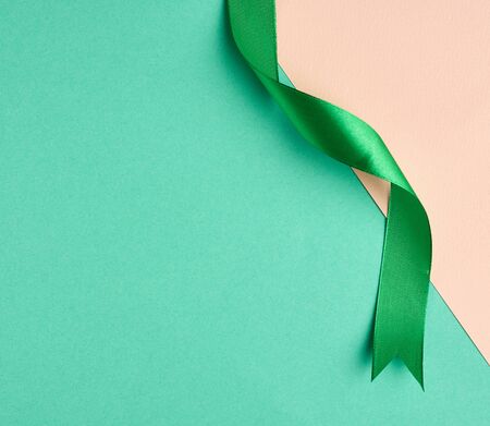 twisted silk green ribbon on a green-beige background, top view, cropped endの写真素材