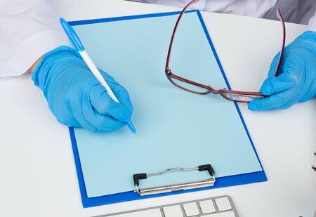 woman doctor in a white coat, sterile medical gloves writes a prescription on a form, therapist sits, workplaceの写真素材