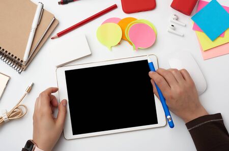 white electronic tablet and two hands, the process of working or drawing on the screen, a workplace...