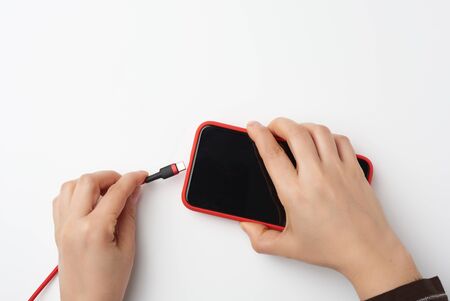 two female hands are holding a smartphone with a blank black screen and cable, charging process,...
