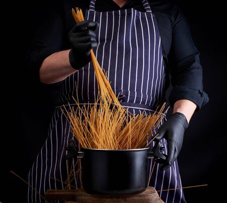 uncooked yellow long spaghetti in a black metal pan and a chef in a striped apron, cooking processの写真素材