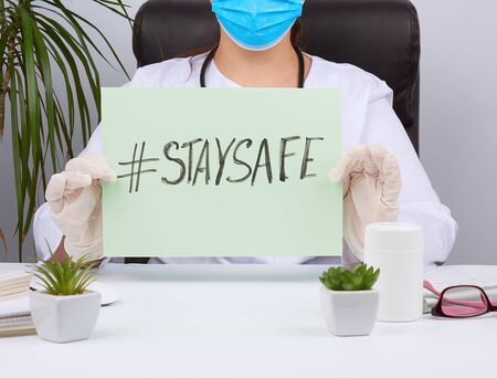 woman doctor in a white coat, sterile medical gloves holds a poster with the inscription stay safe,...
