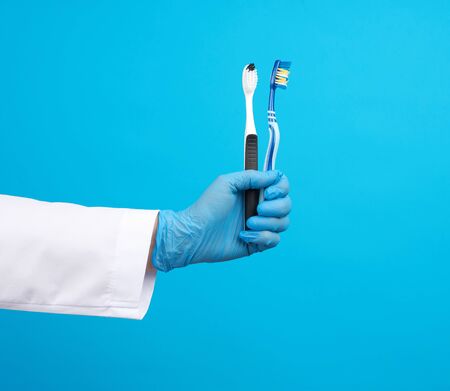 doctor therapist is dressed in a white robe uniform and blue sterile gloves holding a toothbrush, daily brushing concept, blue backgroundの写真素材