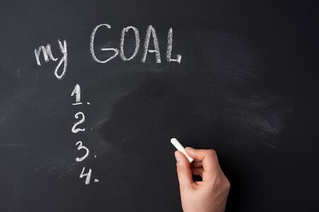 hand holds a white piece of chalk on the background of a chalk board with the inscription my goal