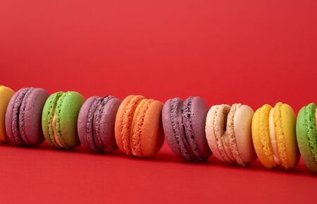 pile of multi-colored baked macarons almond flour cakes on a red background, close upの写真素材