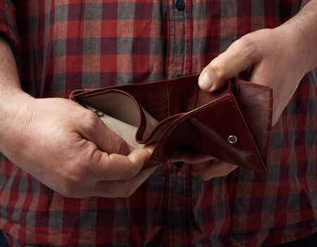 man in a red plaid shirt holds an empty leather brown wallet, concept of poverty and economic crisis
