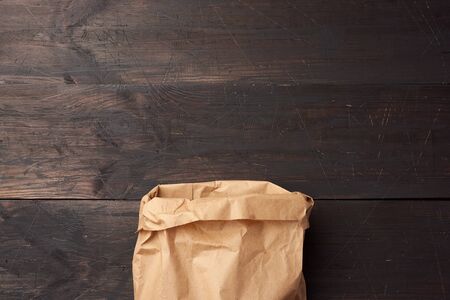 open brown paper bag for food packaging on a brown wooden background, concept of rejection of...