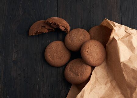 round chocolate chip cookies lie on a brown wooden table, dessert spilled out of a paper bag, top viewの写真素材