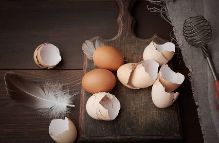 brown raw chicken eggs, shells, cutting board and hand-held whisk for protein on a wooden table, top...
