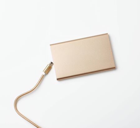 golden power bank and cord with a usb connector for recharging mobile devices on a white background, top viewの写真素材