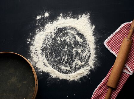 white wheat flour scattered on a black table and a wooden rolling pin on a black table, top viewの写真素材