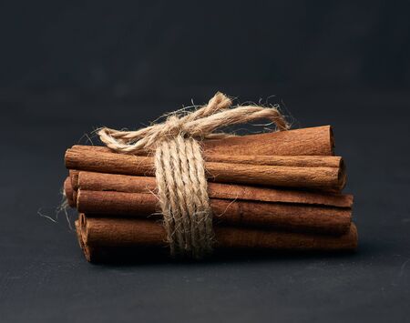 tied bunch of brown cinnamon sticks on a dark background, close upの写真素材