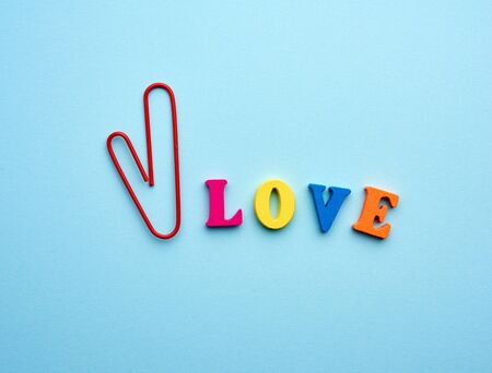 word love made of multi-colored wooden letters and a red paper clip in the shape of a heart on a blue background, top viewの写真素材